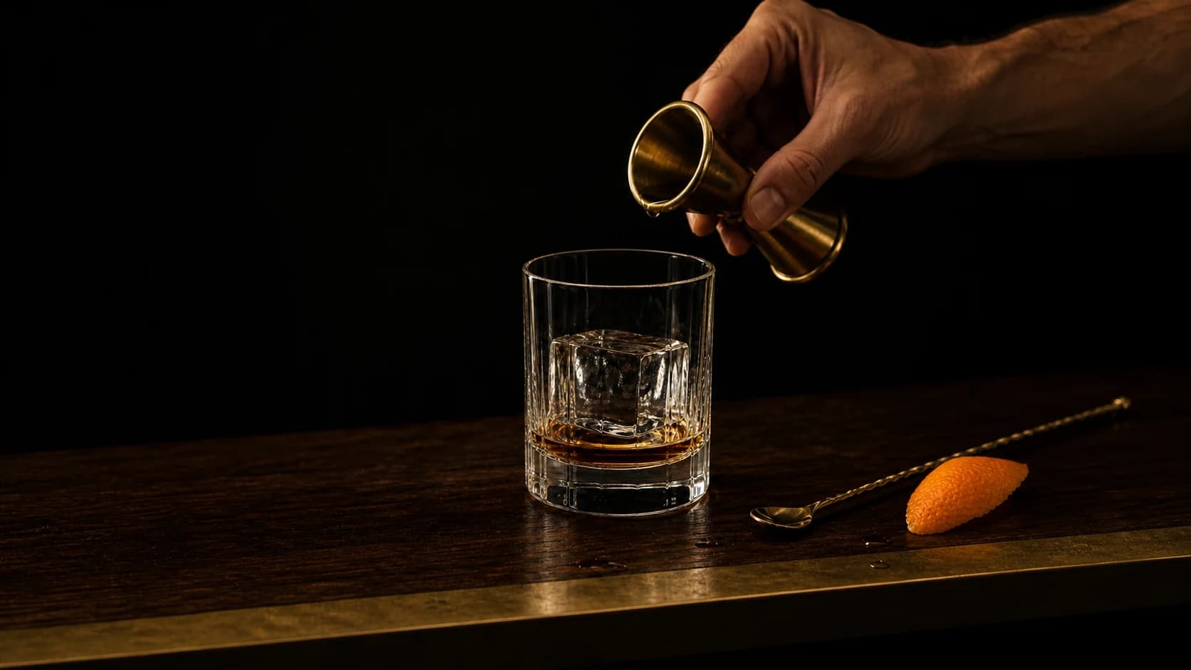 A bartender pouring a measured drink into a rocks glass